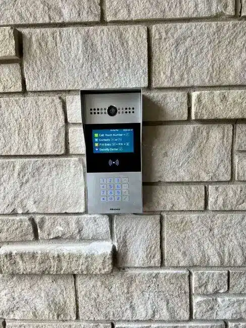 Akuvox video intercom with a call button, contacts screen and keypad on a stone wall, part of connected security systems
