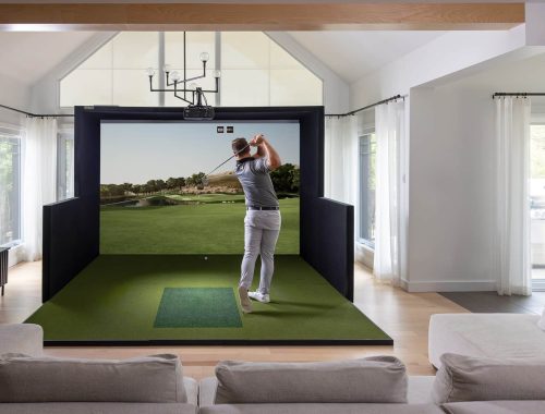 Golfer mid-swing in a SimBooth golf simulator enclosure in a bright living room